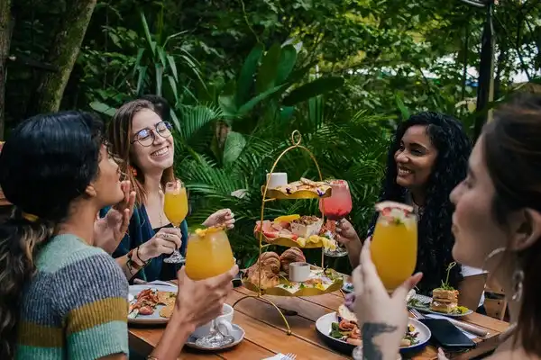 Grupo de amigas celebrando una despedida de soltera en un restaurante, con comida sobre la mesa y levantando sus copas para brindar.