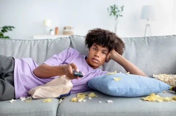 Niño acostado en el sofá viendo televisión, sosteniendo el control remoto en la mano en una postura relajada.