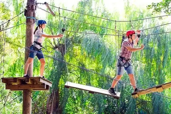 Pareja cruzando un puente de cuerdas en un circuito de obstáculos en los árboles en Parque Arví, Medellín, rodeados de naturaleza.