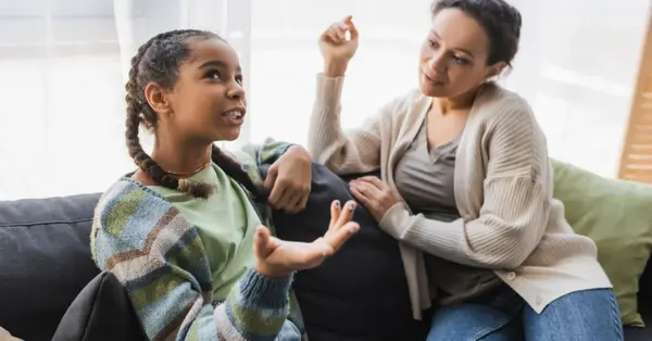Madre y adolescente conversando con respeto en casa, sentados frente a frente y dialogando de forma tranquila.