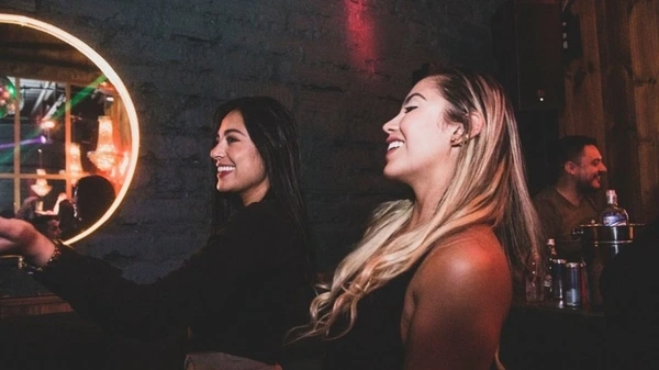 Dos mujeres riendo en un bar privado durante una despedida de soltera en Medellín, disfrutando un momento íntimo y alegre juntas.