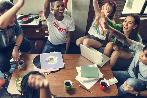 Grupo de niños participando en una actividad en interior, riendo y levantando la mano para responder preguntas en un entorno dinámico y colaborativo.