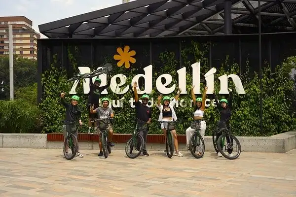 Grupo de turistas posando con sus bicicletas de alquiler frente a un letrero de “Medellín” durante un recorrido en bicicleta por la ciudad.