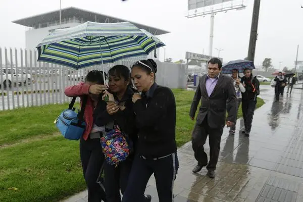 Tres amigos caminando juntos bajo un paraguas durante una fuerte lluvia en Medellín, Colombia, protegiéndose mientras recorren la ciudad.