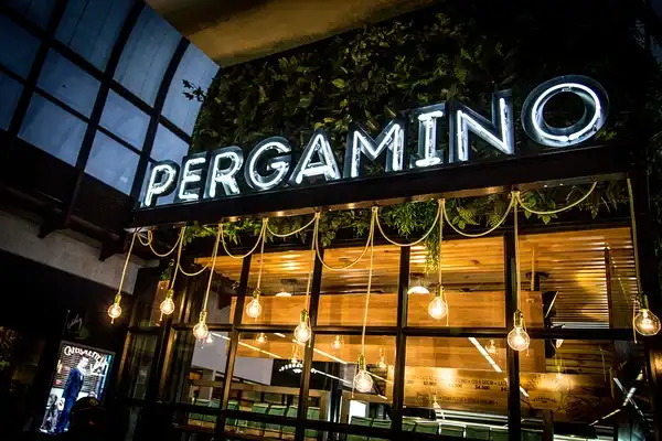 Fachada de Pergamino Café iluminada por la noche, con bombillas rústicas colgantes y ambiente acogedor en la calle.