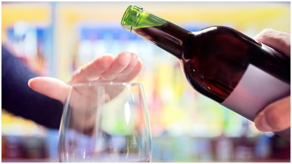 Persona intentando servir vino en una copa mientras el invitado cubre la parte superior del vaso con la mano para indicar que no quiere más.