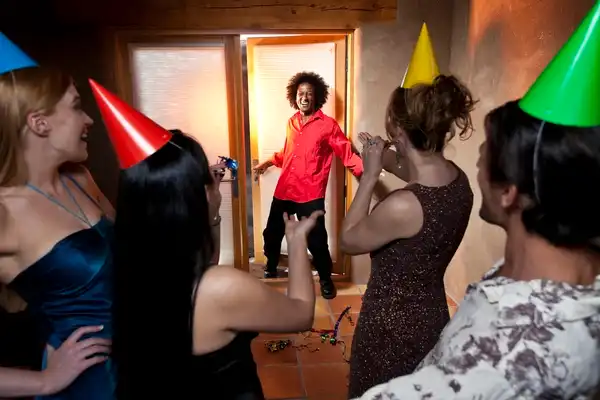 Hombre entrando a una habitación mientras sus amigos se preparan para sorprenderlo en una fiesta sorpresa de cumpleaños.