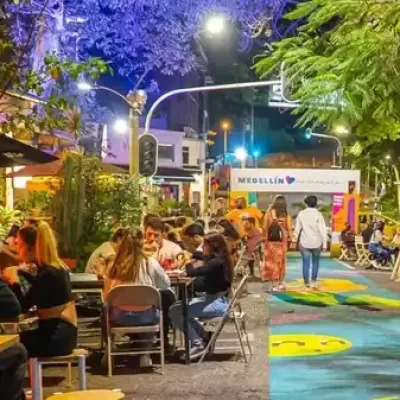 Calle peatonal junto a Parque Lleras en Medellín con personas sentadas en mesas al aire libre, conversando y riendo en bares y restaurantes.