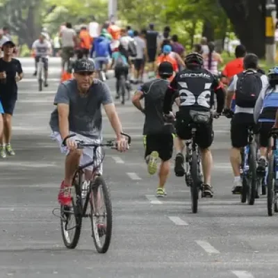 Calle cerrada al tráfico durante la ciclovía en Medellín, con familias caminando juntas y un hombre pasando en bicicleta entre los peatones.