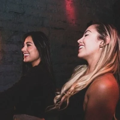 Dos mujeres riendo en un bar privado durante una despedida de soltera en Medellín, disfrutando un momento íntimo y alegre juntas.